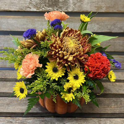 Mixed bouquet in a pumpkin-shaped vase with yellow, orange, purple, and red flowers