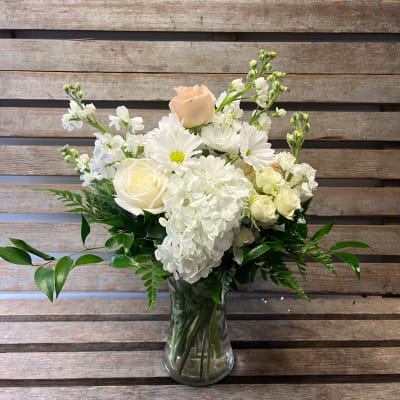 White floral arrangement in a clear glass vase with roses and daisies