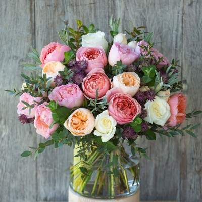 Arrangement of pink, peach, and white roses with purple accents in a clear glass vase