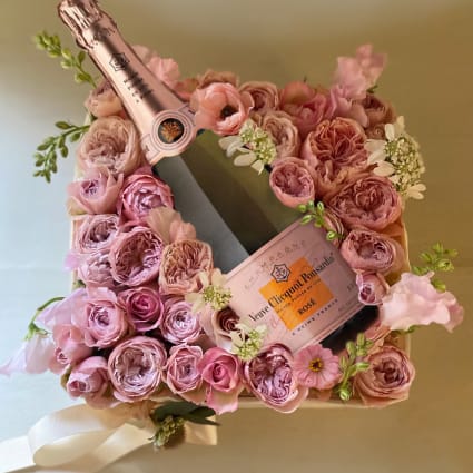 Pink rose arrangement with two champagne bottles in a gift box