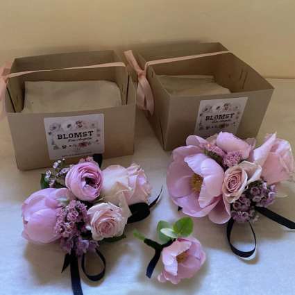 Pink floral boutonnieres and corsages with ribbon ties beside gift boxes