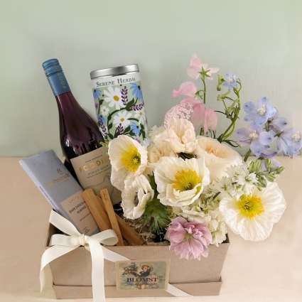 Gift box with flowers, wine, and chocolate bar tied with a white ribbon