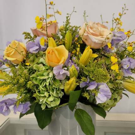 Pastel bouquet of roses, hydrangeas, and yellow orchids in a white vase