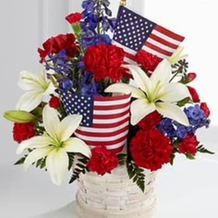 Red, white, and blue floral arrangement in a white basket with American flags