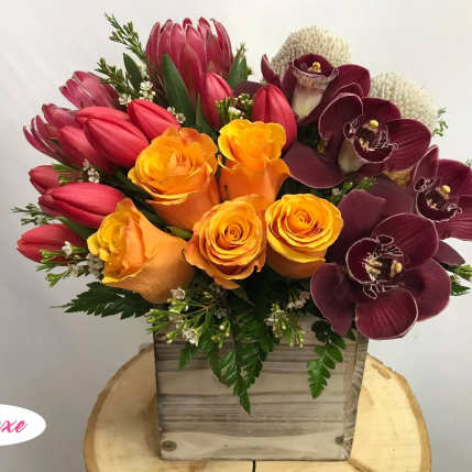 Bouquet of orange roses, red tulips, and burgundy orchids in a wooden box