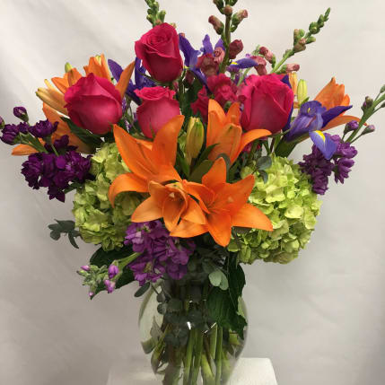 Bright mixed bouquet with orange lilies, pink roses, purple flowers, and green hydrangeas in a glass vase