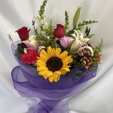 Mixed bouquet with a sunflower, roses, lilies, and purple wrapping