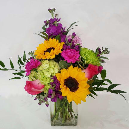 Mixed bouquet with sunflowers, roses, and purple blooms in a clear glass vase