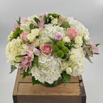 Round arrangement of white hydrangeas, pink roses, and green button mums in a clear vase