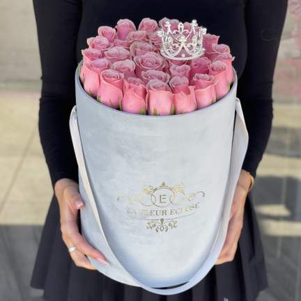 Pink roses arranged in a round hatbox with a small crown topper