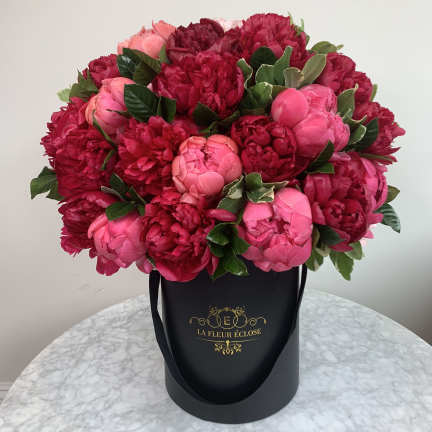 Pink and red peonies arranged in a black hatbox