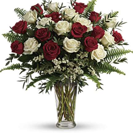Tall arrangement of red and white roses with ferns in a clear glass vase