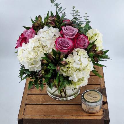 Pink roses and white hydrangeas in a glass vase with a small candle beside it.