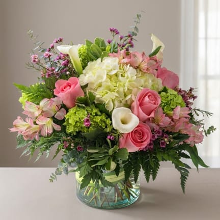 Pink roses, white hydrangea, calla lilies, and mixed blooms in a glass vase