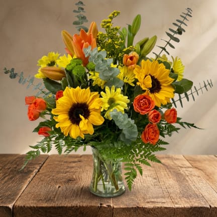 Bouquet of yellow sunflowers and orange roses in a clear glass vase