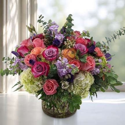 Mixed bouquet of roses, hydrangeas, and purple blooms in a glass vase