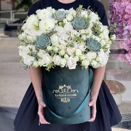 Large white rose and succulent arrangement in a dark green hatbox
