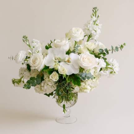 White floral arrangement in a clear glass vase with roses and orchids