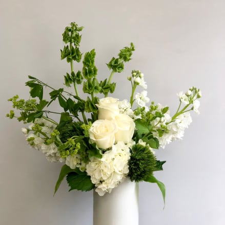 Tall white and green floral arrangement with roses and hydrangeas in a white vase