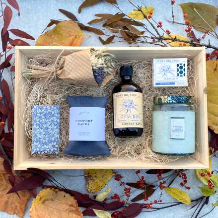 Wooden gift box with dried bouquet, candle, soaps, bubble bath, and comfort pack on autumn leaves