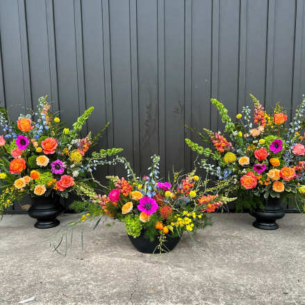 Trio of large bright orange, pink, yellow, and purple flower arrangements in black urn and bowl vases