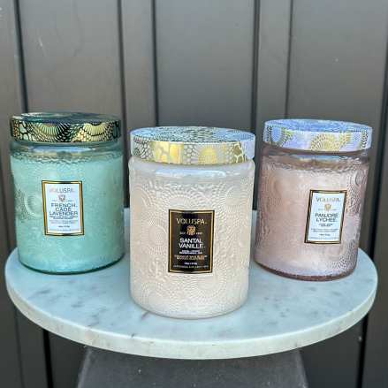 Three large decorative glass jar candles with patterned lids on a round marble stand