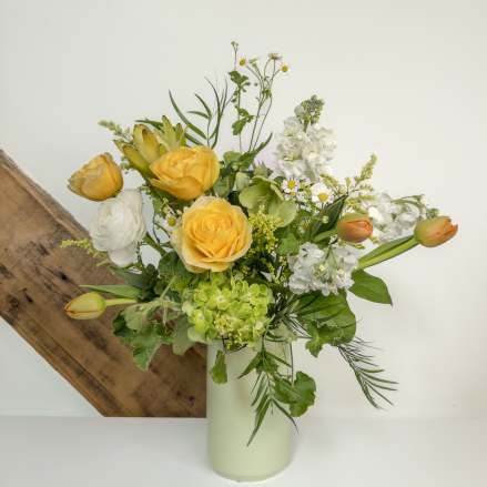 Tall arrangement of yellow roses, white flowers, green hydrangea and tulips in a pale vase