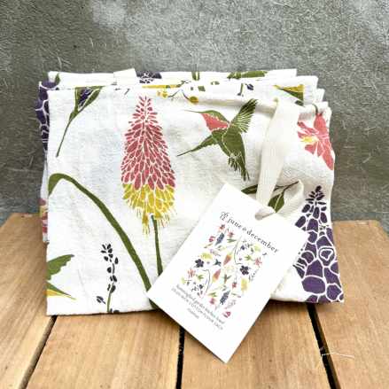 Folded white cotton towel with colorful floral and hummingbird print and hanging tag.