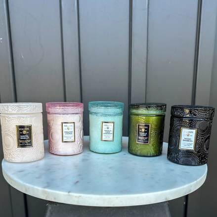 Set of five embossed glass jar candles in assorted colors on a round marble stand.