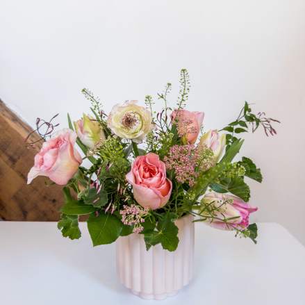 Pink and white flower arrangement with roses in a pale ribbed vase on a white surface