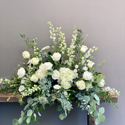 Large white and green floral arrangement with roses and hydrangeas on a wooden stand