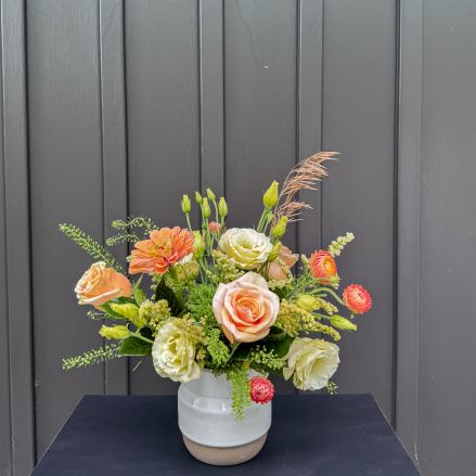 Mixed bouquet of peach, cream, and orange flowers in a white ceramic vase