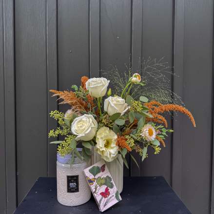 White roses and pale blooms in a vase with a candle and gift box