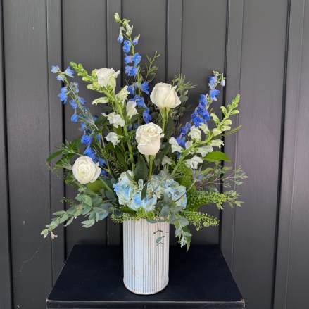 Tall arrangement of white roses and blue flowers in a ribbed white vase