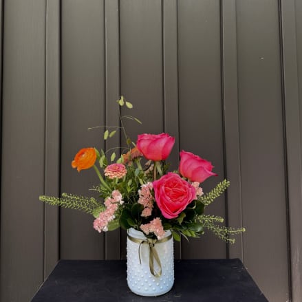 Pink and orange flowers arranged in a white textured vase with a ribbon.