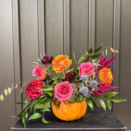 Mixed bouquet in a pumpkin-shaped orange container with pink, orange, and burgundy flowers