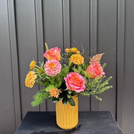 Pink and orange roses with yellow blooms in a tall yellow vase