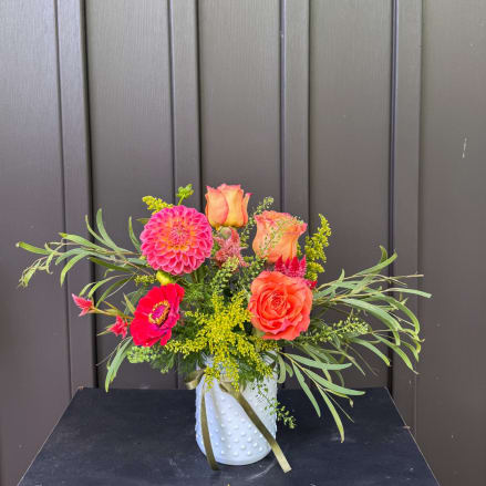 Bright mixed bouquet in a white textured vase with roses and dahlias