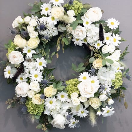 White and cream floral wreath with roses, daisies, and hydrangeas on a gray background