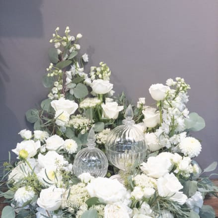 Low white flower arrangement with roses and mums surrounding two clear glass lidded jars.