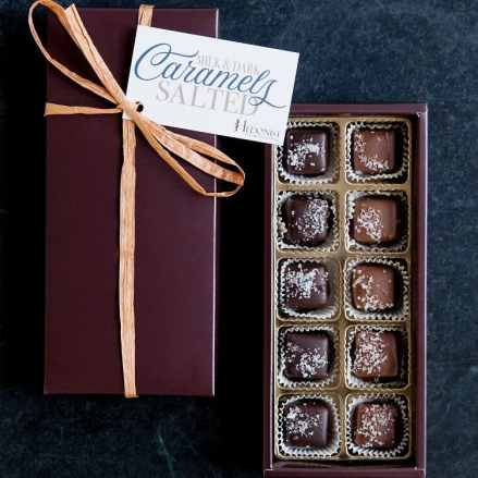 Rectangular gift box of salted caramels with ribbon and open tray showing assorted chocolates.