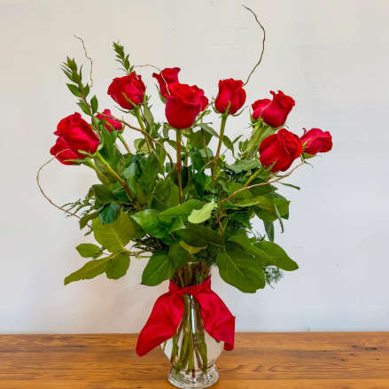 Tall arrangement of red roses in a clear glass vase with a red ribbon bow