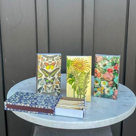 Decorative matchboxes with botanical and butterfly designs on a round marble table