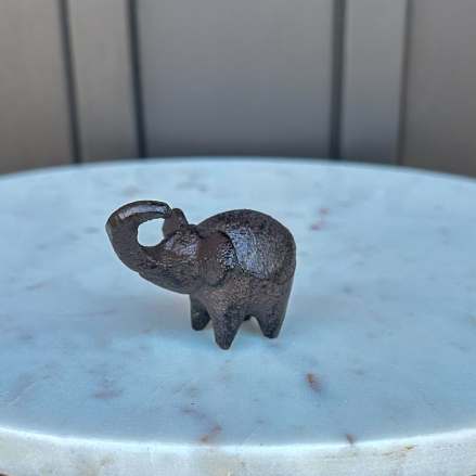 Small dark metal elephant figurine on a round white marble surface