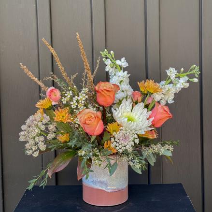 Mixed bouquet of peach roses, white blooms, and orange flowers in a ceramic vase