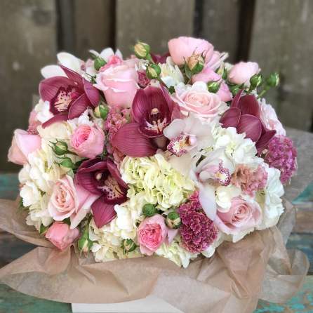 Pink and white bouquet with roses, orchids, and hydrangeas wrapped in paper