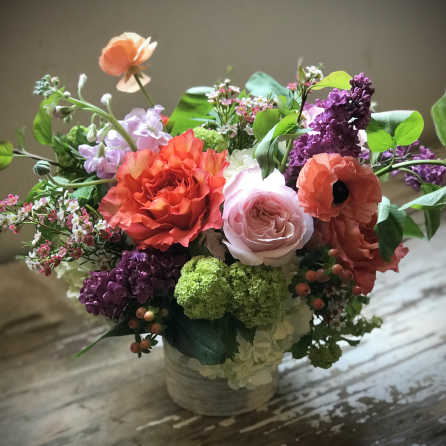 Mixed bouquet of coral, pink, purple, and white flowers in a low container
