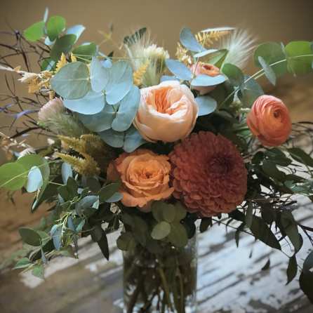 Peach and coral bouquet in a glass vase with blue-green foliage