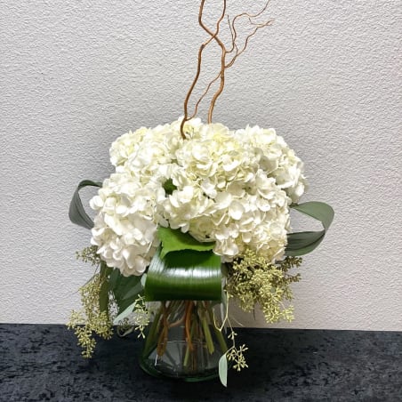 White hydrangea arrangement with structured green leaves in a clear glass vase and curly willow branches