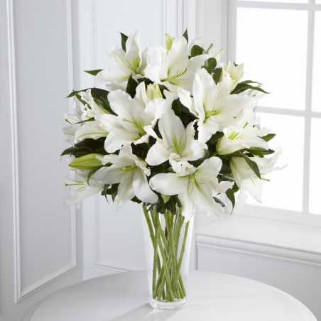 Tall clear vase filled with large white lilies on a round white table
